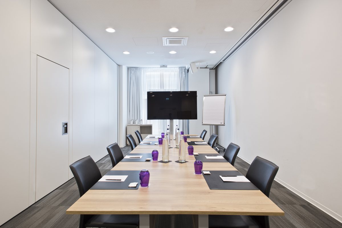 Bright meeting room with a long wooden table, screen and flipchart, set up for a workshop