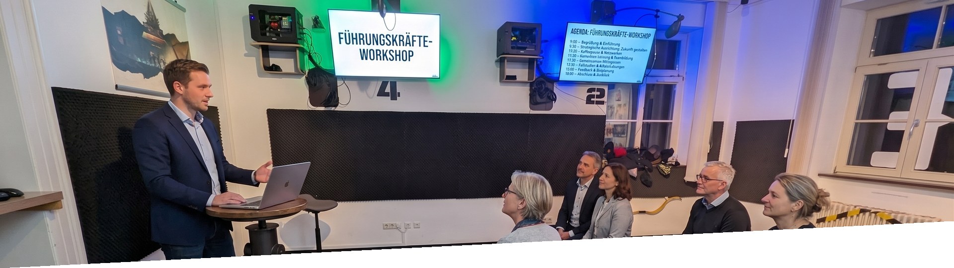 Leadership team in a workshop: consultant at a lectern, participants in a semicircle, screen showing the title Leadership Workshop